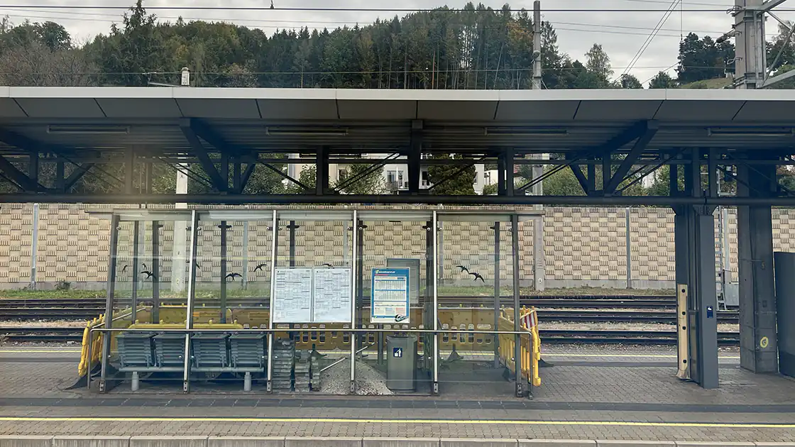 Im Bild zu sehen ist der Bahnsteig 2/3 des Bahnhof Vöcklabruck in Oberösterreich. Im Hintergrund sind weitere Bahngleise zu sehen. Außerdem sieht man in der Bildmitte ein Wartehäuschen mit Sitzgelegenheiten.