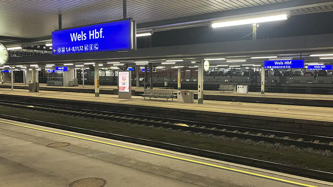 Der Hauptbahnhof Wels bei den Bahnsteigen während einer Fahrt am Abend fotografiert. Die Gleise wirken leer.