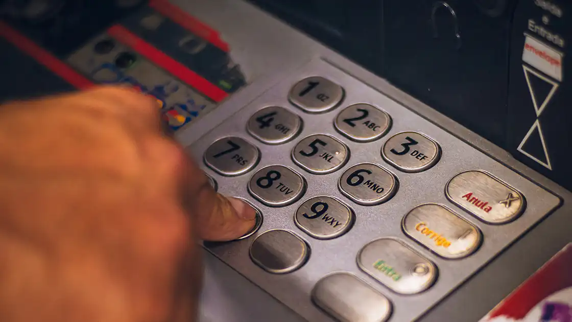 Das Bild zeigt eine Nahaufnahme von einem Bankomat-Gerät, wo eine Person gerade einen PIN-Code eintippt. Der Geheimcode ist notwendig um Bargeld von einem Automaten abheben zu können, daher ist der PIN-Code auch begehrt bei Dieben.