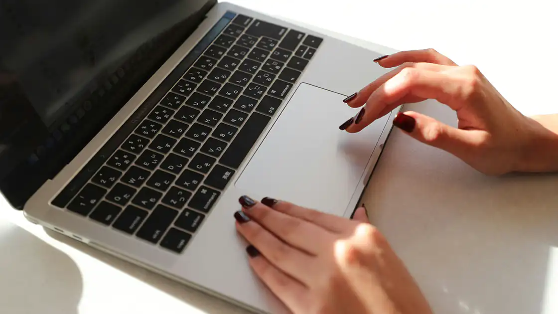 Eine Frau mit lackierten Fingernägeln tippt au feinem Laptop, der Monitor ist schwarz, mit den Händen berührt sie das Touch-Pad des Gerätes, das als Maus-Ersatz dient.