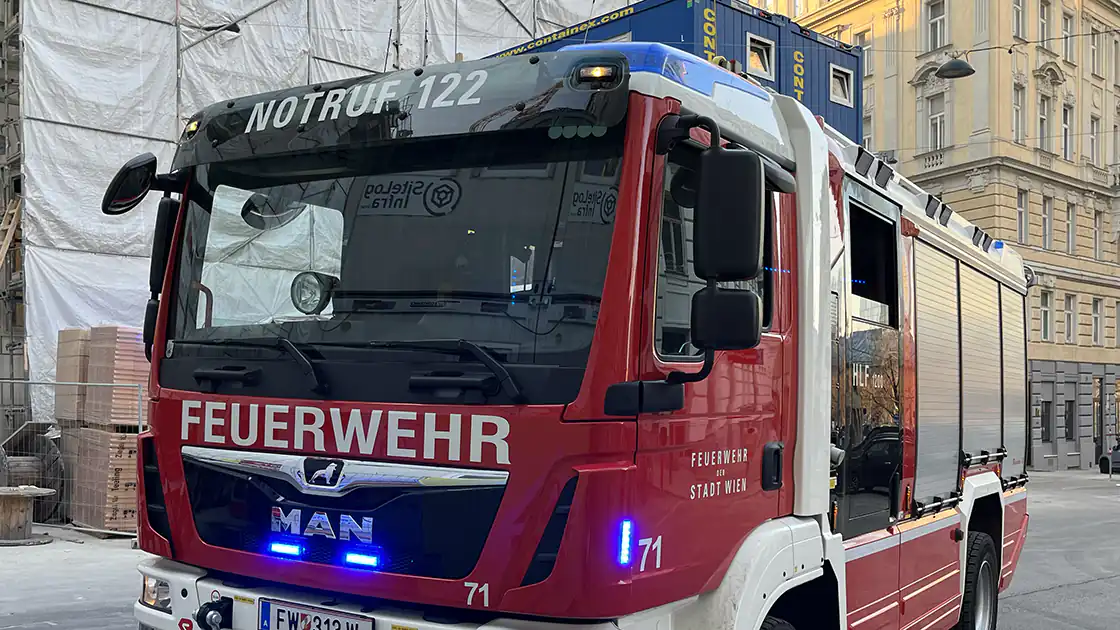 Ein großes Feuerwehrfahrzeug mit aufgedruckter Notrufnummer ist hier im Einsatz. Das Blaulicht ist eingeschaltet, das Feuerwehrauto fährt auf die Kamera zu.