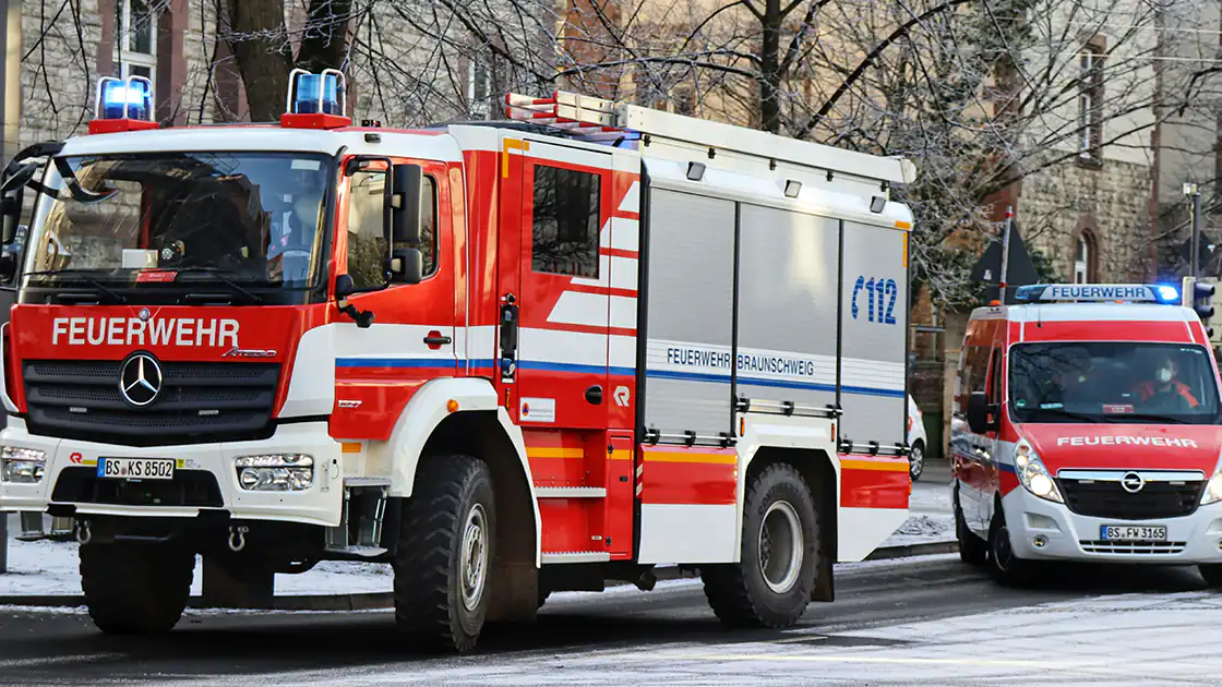 Mehrere Fahrzeuge der Feuerwehr sind hier im Einsatz. Die Fahrzeuge haben das Blaulicht eingeschaltet. Das hintere, kleinere Fahrzeug der Feuerwehr fährt gerade weg.