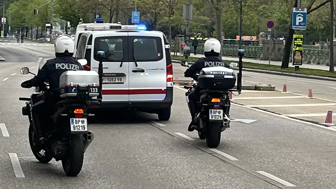 Zu vielen Einsätzen der Polizei werden neben Polizeiautos auch Motorräder der Polizei eingesetzt. In diesem Bild begleiten zwei Polizeimotorräder ein Polizeifahrzeug auf einer großen Straße.