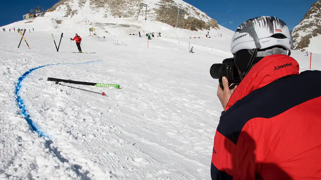 Nach einem Skiunfall oder Alpinunfall ist die Polizei hier im Einsatz bei den Erhebungen zum Fall zu sehen. Es werden Bilder gemacht, eine Person im Vordergrund analysiert die Szene. Entsprechende Bodenmarkierungen in einer Spur im Schnee wurden vorgenommen.
