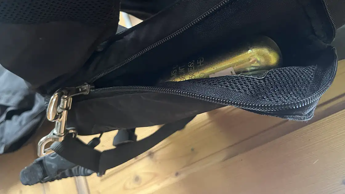 Das Bild zeigt eine Schutzweste zum Reiten mit einem eingebauten Airbag. Seitlich ist ein Reisverschluss geöffnet und man sieht die goldene Gasflasche, die in der Jacke eingebaut ist. Außerdem ist die Leine zu sehen mit der man die Schutzweste am Sattel befestigt um den Airbag auszulösen, sobald man vom Pferd fällt.