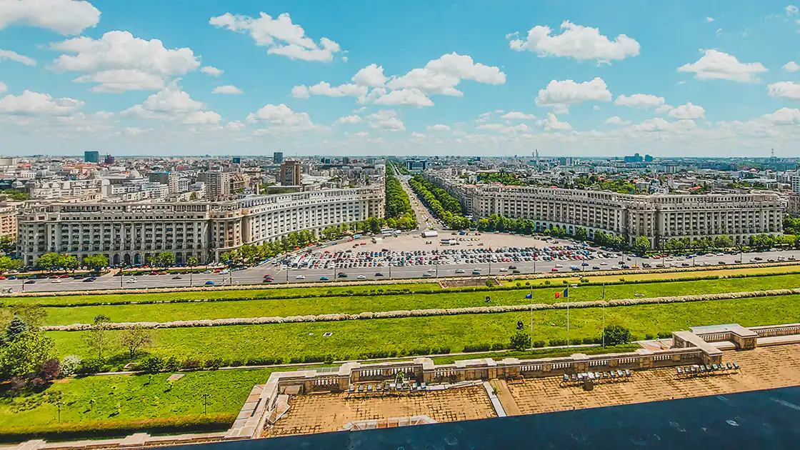 Ein riesiger Palast mit vielen Fenstern ist hier in der rumänischen Hauptstadt Bukarest zu sehen. Vor dem Palast ist ein großer grüner Park.
