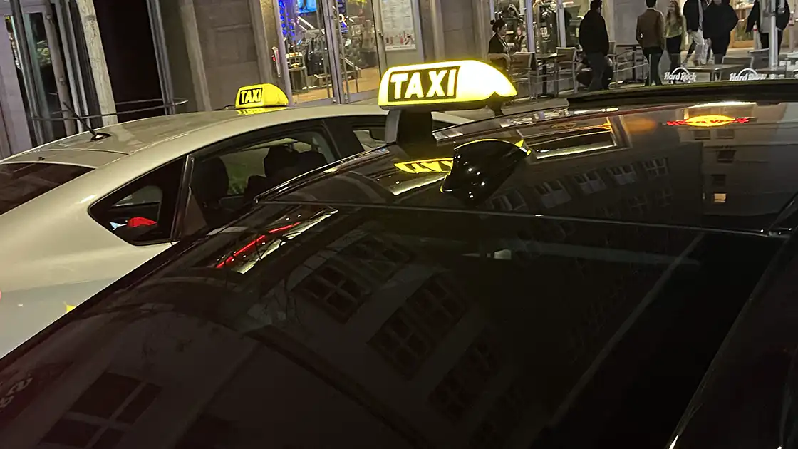 Taxi- und Fahrdienste sind überall im Einsatz. Dieses Bild zeigt mehrere Taxis mit den leuchtenden Taxi-Schildern auf dem Autodach in einer Abendstimmung in einer Stadt.