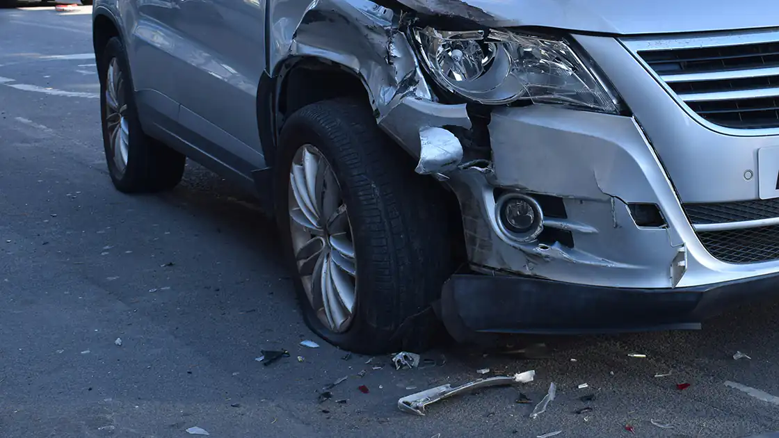 Nach einem Unfall ist ein Auto auf der rechten Seite an der Front stark beschädigt. Das Fahrzeug hat den Kotflügel verloren, das Licht ist zertrümmert und der Reifen ist kaputt.