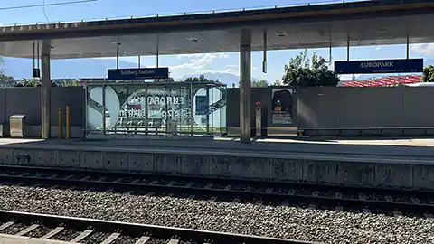 Am Bild sind zwei Gleise und dann der zweite Teil des Bahnhofsgebäudes in Salzburg Taxham beim Europark zu sehen. Europark ist ein großes Einkaufszentrum in der Stadt Salzburg.