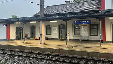 In Kärnten liegt der Bahnhof Treibach-Althofen, er gehört zu den kleineren Bahnhöfen mit überregionalen Verbindungen, hier bleiben auch einige Railjet-Züge stehen. Der Bahnhof Treibach Althofen liegt auf der Strecke zwischen Klagenfurt und Bruck an der Mur (Steiermark). Im Vordergrund ist ein Eisenbahn-Gleis zu sehen, dahinter der Bahnsteig und das Bahnhofsgebäude. Das Gebäude hjat ein Stockwerk und oben ein Gibeldacht. Es sind die Eingänge zur Bahnhofsverwaltung, zum Wartezimmer und auch zu den Toiletten zu sehen.