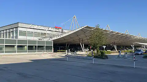 Auf dem Symbolbild hier ist das Flughafen-Hauptgebäude vom Salzburg Airport Wolfgang Amadeus Mozart zu sehen. Darin sind die Terminals 1 und 2 untergebracht, im Gebäude befindet sich unten der Check-In-Bereich und es gibt auf der gegenüberliegenden Seite eine schöne Dachterrasse, die den Blick auf das Flugfeld bietet. Der Flughafen in Salzburg ist ein Regionalflughafen mit internationalen Verbindungen.