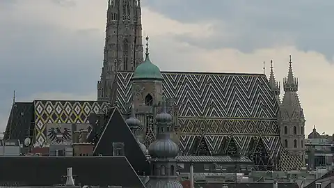 Seitliche Ansicht vom Wiener Stephansdom. Der Stephansdom in Wien ist das zentrale Wahrzeichen der Stadt im ersten Bezirk. Man sieht nicht den ganzen Stephansdom sondern nur das Hauptschiff und den unteren Teil des Kirchturmes. Davor sind einge Dächer anderer Häuser zu sehen, die Aufnahme wurde vom Dach eines Hauses im Norden des 1. Bezirks mit Blickrichtung Süden gemacht.